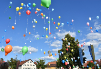 Viele bunte Luftballons mit Zetteln steigen auf in einen weiß-blauen Himmel auf