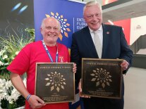 Zwei Männer mit Plakette mit stilisierter Blüte posieren fürs Foto
